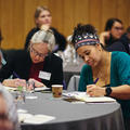 Two women sat at a table writing in notebooks at a conference