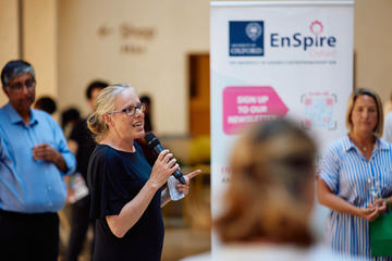 Kylie Vincent talking at the Demo Night 2023 event with an EnSpire banner and crowd members in the background