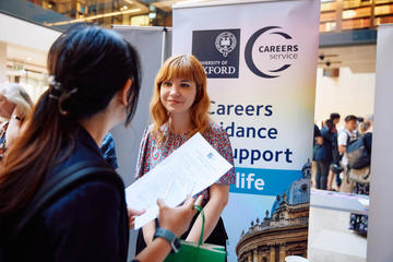 The Careers Services, University of Oxford team member stood next to their stand and chatting to Demo Night attendee