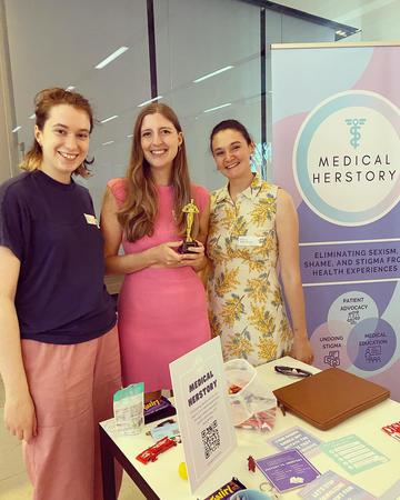 Demo Night 2023 third place winners, Medical Herstory stood next to their stand holding a trophy